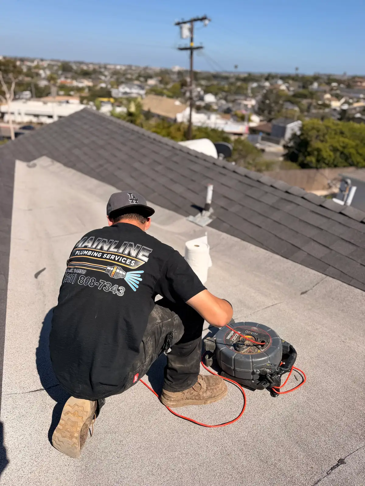 Mainline Plumbing technician running a sewer camera down a rooftop vent stack above a South Bay neighborhood