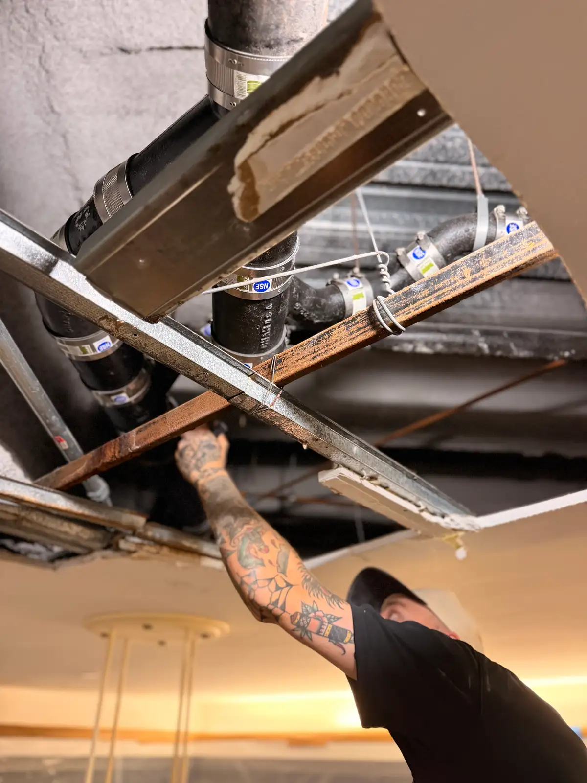 Mainline Plumbing technician installing a new cast iron drain line with no-hub couplings in an open commercial ceiling