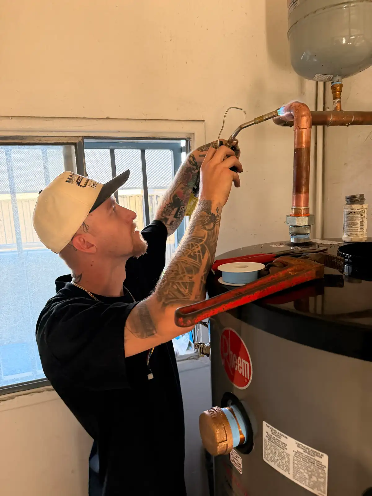 Mainline Plumbing technician soldering a copper water line above a newly installed Rheem water heater in the South Bay