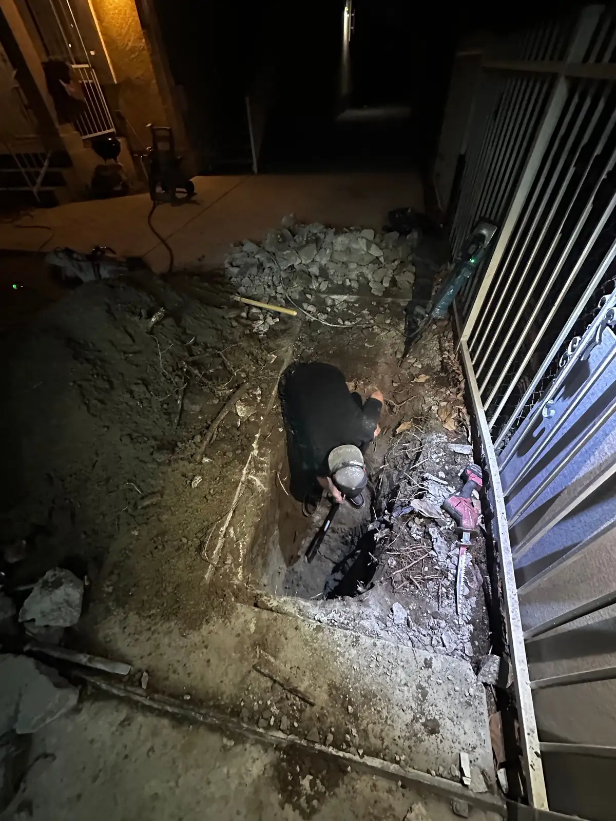 Mainline Plumbing technician working inside an excavated sewer pit at night during an after-hours emergency call in the South Bay